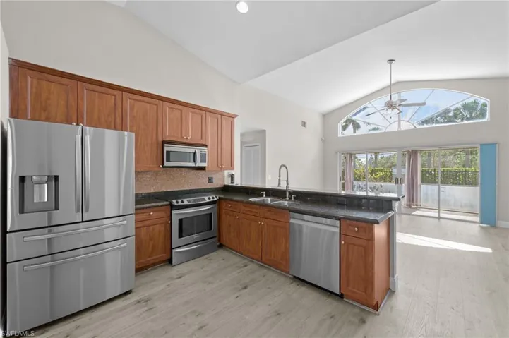 Kitchen featuring stainless steel appliances, wood finish cabinetry, vaulted ceiling, a peninsula, and light wood finished floors