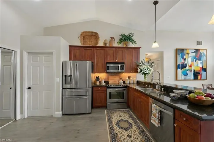 Kitchen with stainless steel appliances, dark stone counters, a peninsula, vaulted ceiling, and pendant lighting