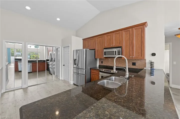 Kitchen featuring wood finish cabinets, dark stone countertops, lofted ceiling, light wood finished floors, and stainless steel appliances