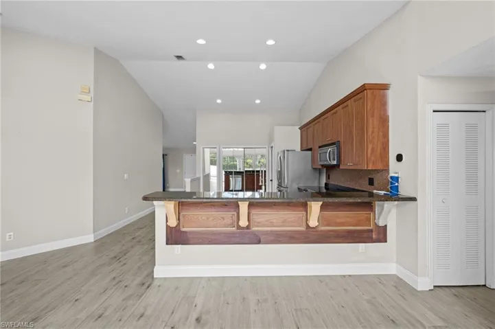 Kitchen featuring a breakfast bar, wood finish cabinetry, vaulted ceiling, light wood-style flooring, and a peninsula