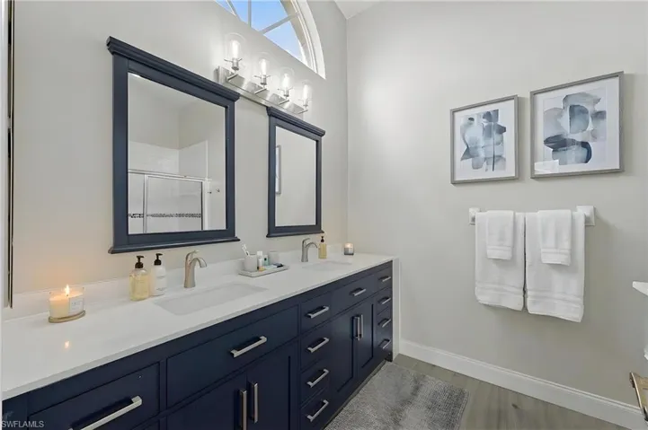 Full bathroom with double vanity, a stall shower, and light wood-style flooring