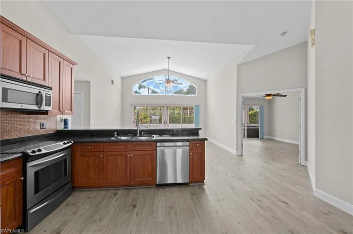 Kitchen with stainless steel appliances, lofted ceiling, ceiling fan, light wood-style flooring, and a peninsula