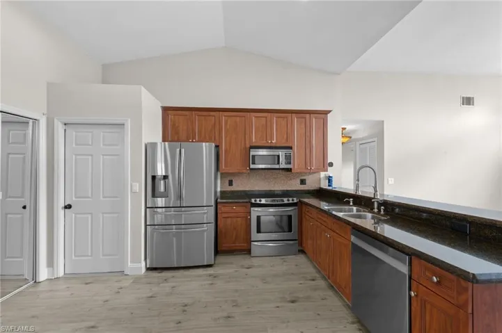 Kitchen with dark stone counters, stainless steel appliances, wood finish cabinets, light wood-style floors, and lofted ceiling