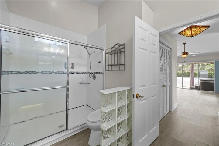 Bathroom featuring light wood finished floors, a stall shower, a ceiling fan, and a closet