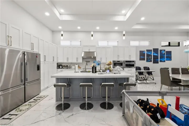 Two tone kitchen featuring stainless steel appliances, a breakfast bar area, a spacious island, decorative light fixtures, and a raised ceiling
