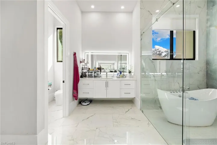 Bathroom with light marble finish flooring, vanity, a freestanding tub, and recessed lighting