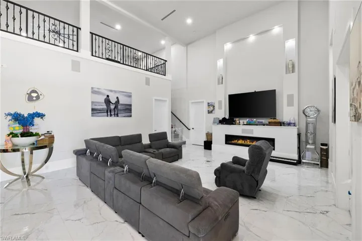 Living room featuring a warm lit fireplace, recessed lighting, a high ceiling, and light marble finish flooring