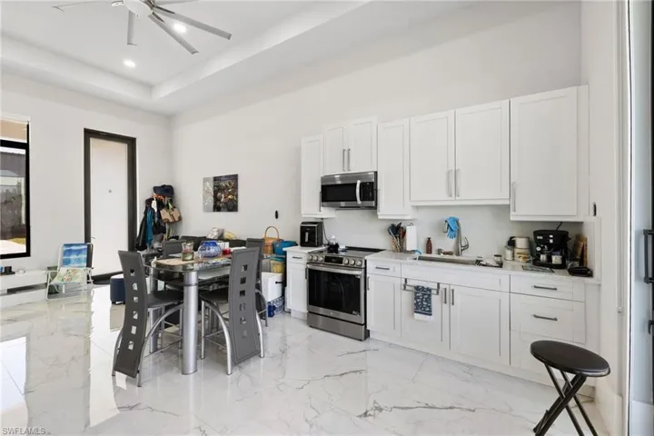 Kitchen featuring stainless steel appliances, white cabinets, a ceiling fan, light stone counters, and light marble finish flooring