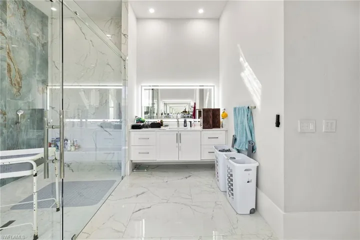 Full bathroom with vanity, a marble finish shower, a high ceiling, and recessed lighting
