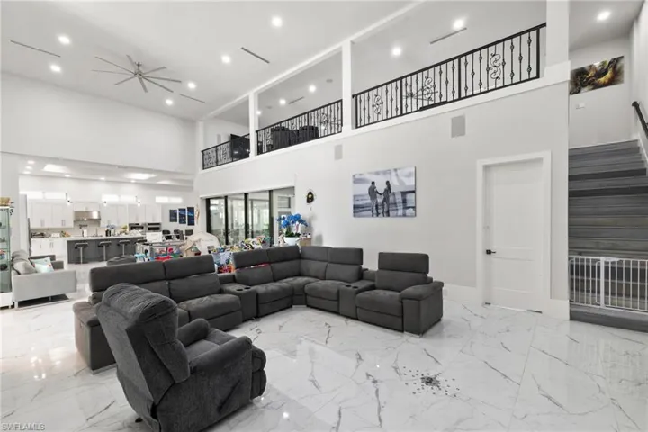 Living room featuring recessed lighting, a ceiling fan, light marble finish flooring, and a high ceiling