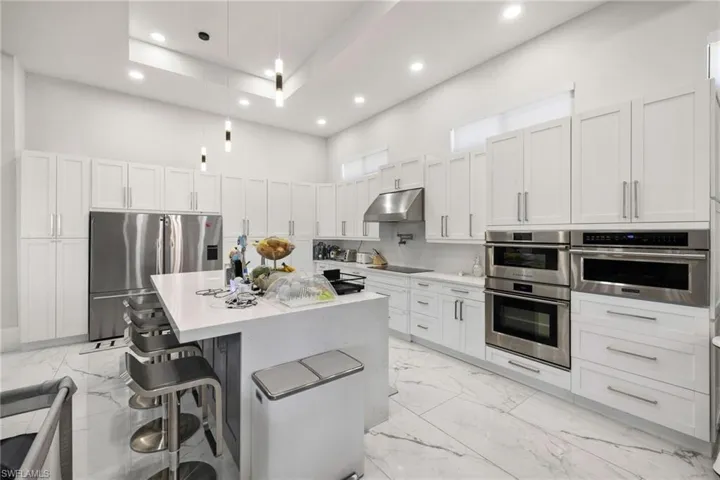 Kitchen with a center island, stainless steel appliances, light stone counters, a kitchen bar, and pendant lighting