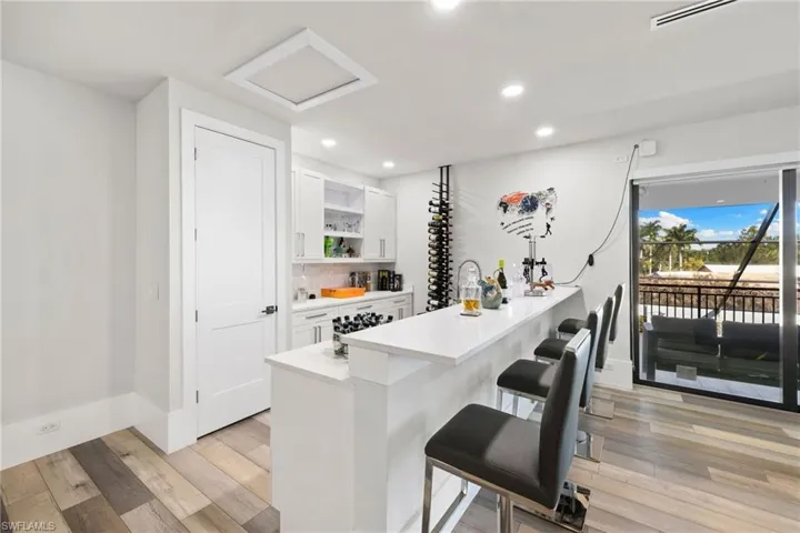 Bar area featuring light wood-style flooring, white cabinetry, open shelves, and recessed lighting