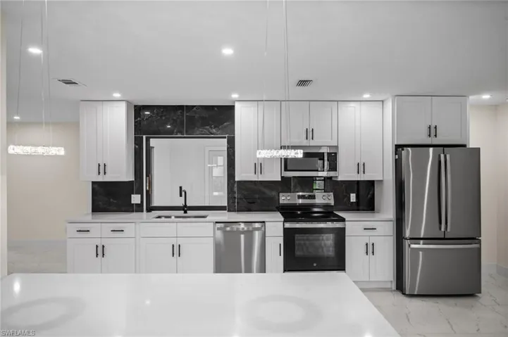 Kitchen with light marble finish floors, appliances with stainless steel finishes, white cabinets, light stone countertops, and recessed lighting
