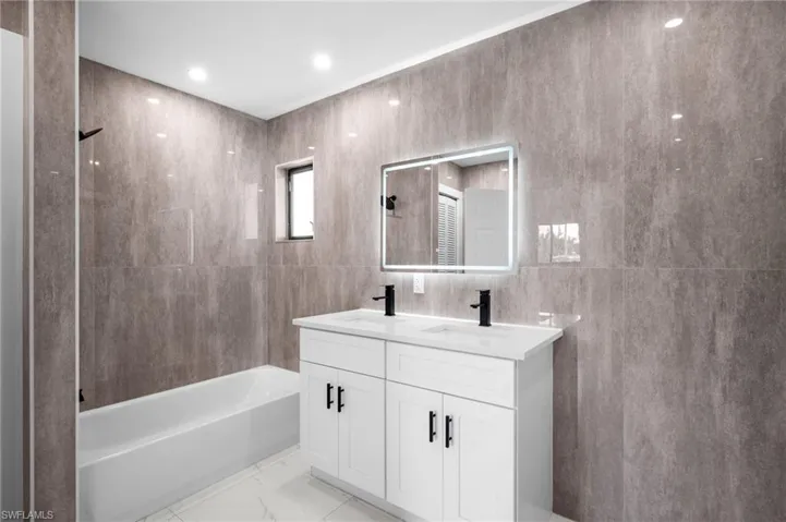 Full bath featuring washtub / shower combination, tile walls, and double vanity