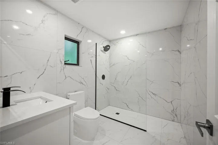 Full bathroom with stone wall, vanity, a marble finish shower, marble tiled flooring, and tile walls