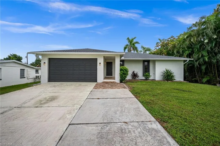 View of front of house with stucco siding, concrete driveway, a front yard, and a garage
