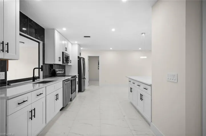 Kitchen featuring white cabinetry, light marble finish flooring, stainless steel appliances, light stone countertops, and recessed lighting