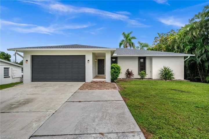 View of front of property with stucco siding, driveway, a front lawn, and a garage