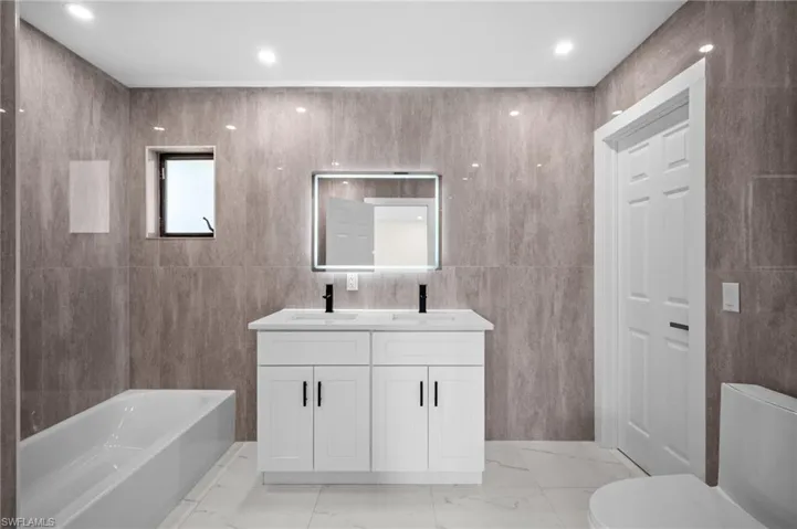 Bathroom with tile walls, a garden tub, double vanity, light marble finish flooring, and recessed lighting