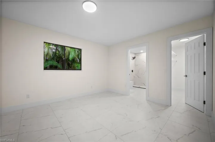 Unfurnished bedroom featuring light marble finish flooring, a spacious closet, and ensuite bath