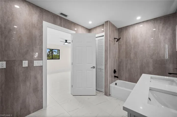 Bathroom with tile walls, bathing tub / shower combination, light marble finish floors, double vanity, and a ceiling fan