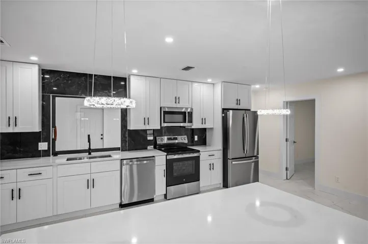 Kitchen with stainless steel appliances, white cabinets, pendant lighting, light marble finish flooring, and recessed lighting