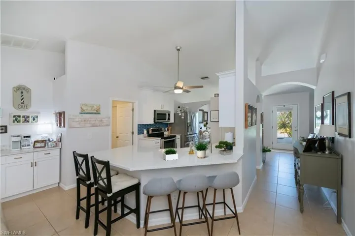 Kitchen with stainless steel appliances, arched walkways, light tile patterned floors, a kitchen breakfast bar, and white cabinetry