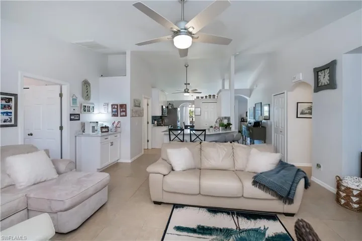 Living area featuring ceiling fan, arched walkways, light tile patterned floors, high vaulted ceiling, and baseboards