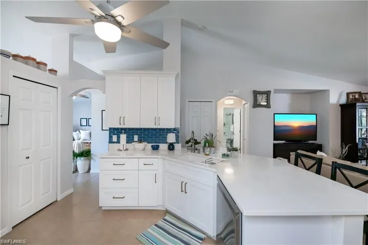 Kitchen with arched walkways, backsplash, a sink, light countertops, and high vaulted ceiling