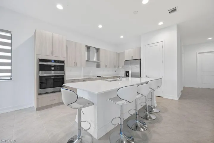 Kitchen featuring a kitchen breakfast bar, a center island with sink, wall chimney exhaust hood, appliances with stainless steel finishes, and sink