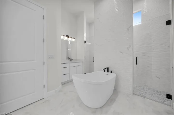 Bathroom with a marble finish shower, marble finish floor, a freestanding tub, and vanity