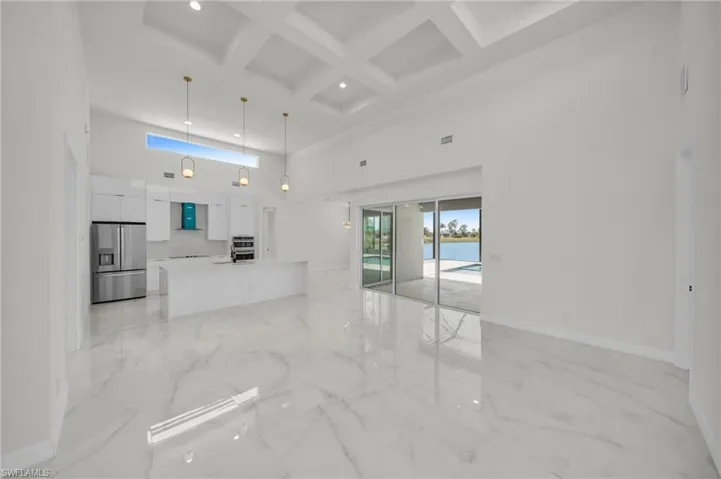 Unfurnished living room featuring beam ceiling, baseboards, marble finish floor, and a high ceiling