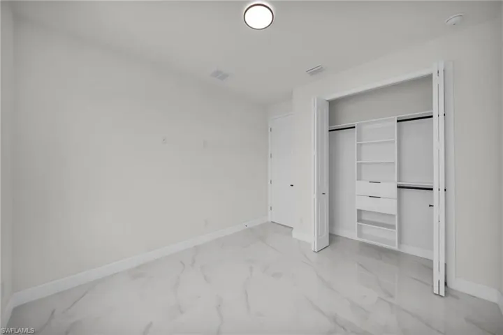Unfurnished bedroom featuring marble finish floor, visible vents, a closet, and baseboards