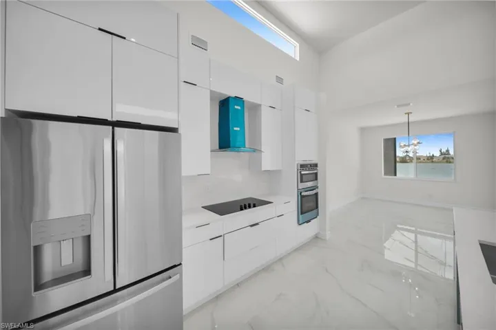 Kitchen with modern cabinets, wall chimney exhaust hood, marble finish floor, white cabinetry, and appliances with stainless steel finishes