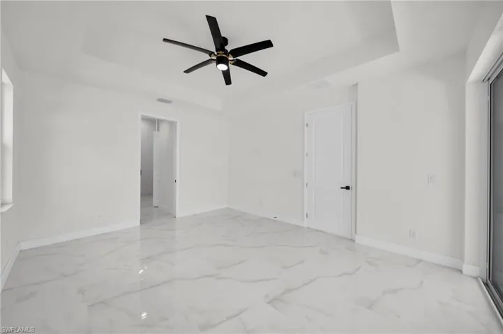 Spare room with a ceiling fan, visible vents, marble finish floor, and a tray ceiling