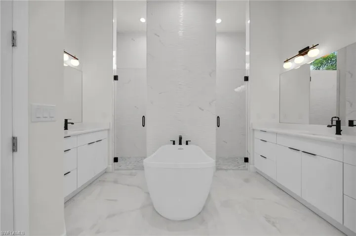 Bathroom featuring a sink, a stall shower, marble finish floor, a freestanding bath, and two vanities