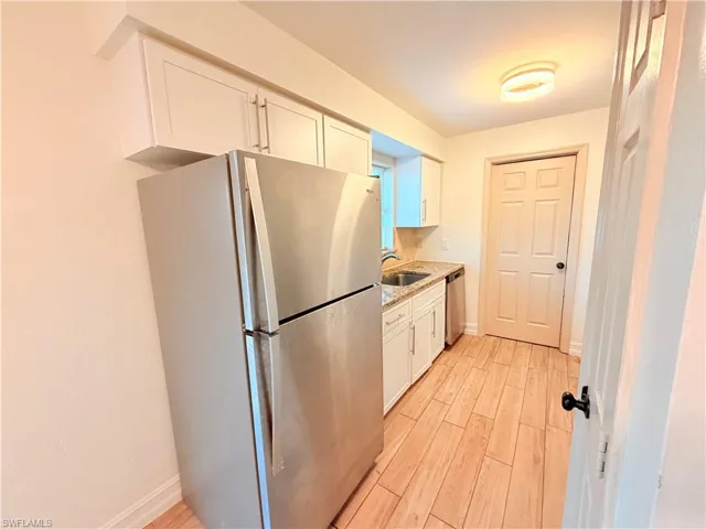 Kitchen featuring stainless steel appliances, white cabinets, light wood-type flooring, and light stone counters