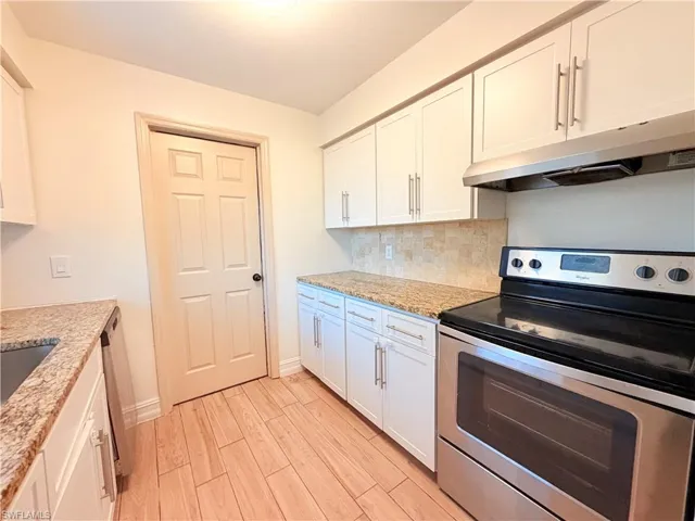 Kitchen featuring stainless steel appliances, light wood finished floors, decorative backsplash, and white cabinets