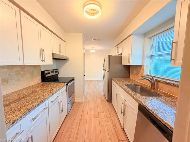 Kitchen featuring stainless steel appliances, light stone counters, white cabinets, and backsplash