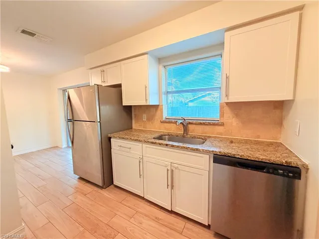 Kitchen featuring stainless steel appliances, backsplash, light stone counters, wood finish floors, and white cabinetry