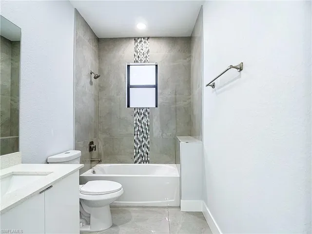 Full bathroom featuring tiled shower / bath, vanity, toilet, and tile floors