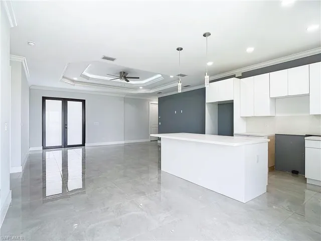 Kitchen featuring pendant lighting, a raised ceiling, a center island, ornamental molding, and white cabinets