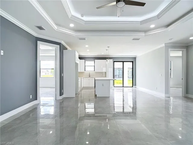 Unfurnished living room with ceiling fan, a raised ceiling, and crown molding