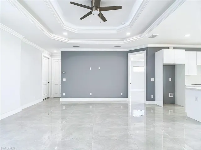 Empty room with ceiling fan, a tray ceiling, crown molding, and light tile floors