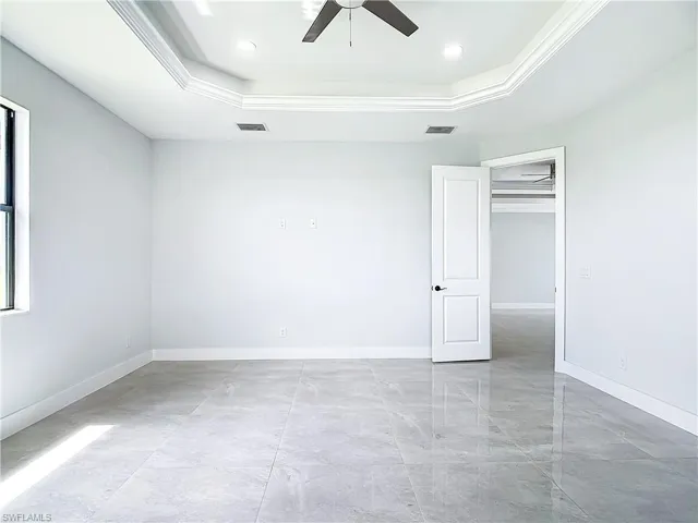 Unfurnished bedroom featuring a tray ceiling, a closet, light tile flooring, and ceiling fan