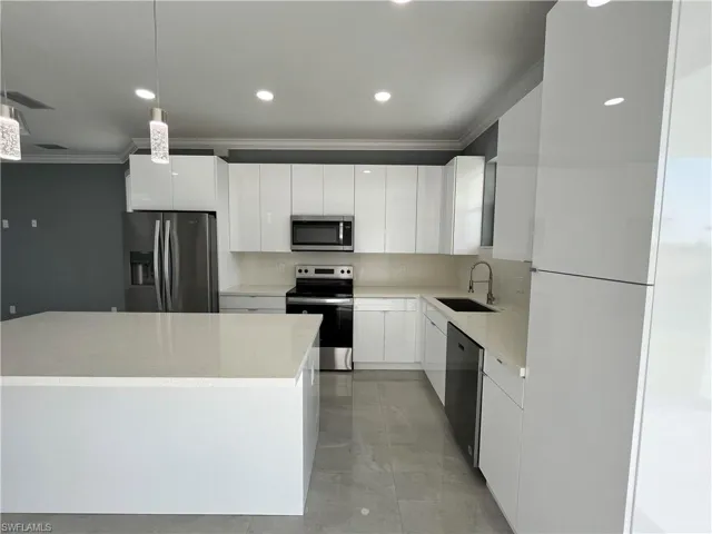 Kitchen with stainless steel appliances, sink, light tile patterned flooring, white cabinetry, and ornamental molding