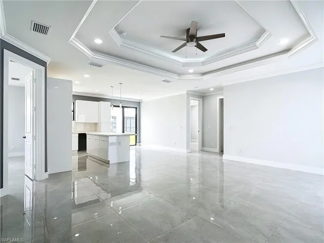 Tiled empty room featuring a tray ceiling, crown molding, and ceiling fan