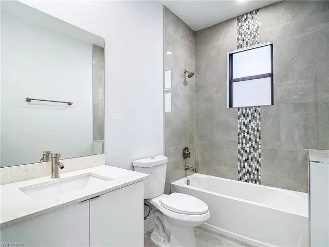 Full bathroom with tiled shower / bath, vanity, toilet, and tile flooring