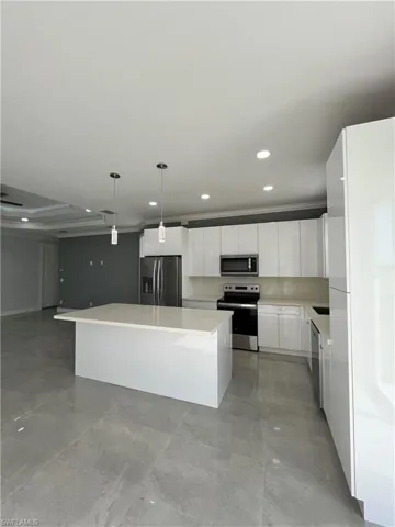 Kitchen featuring decorative light fixtures, white cabinets, ornamental molding, a kitchen island, and appliances with stainless steel finishes
