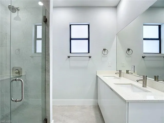 Bathroom with tile floors, a shower with shower door, and dual bowl vanity